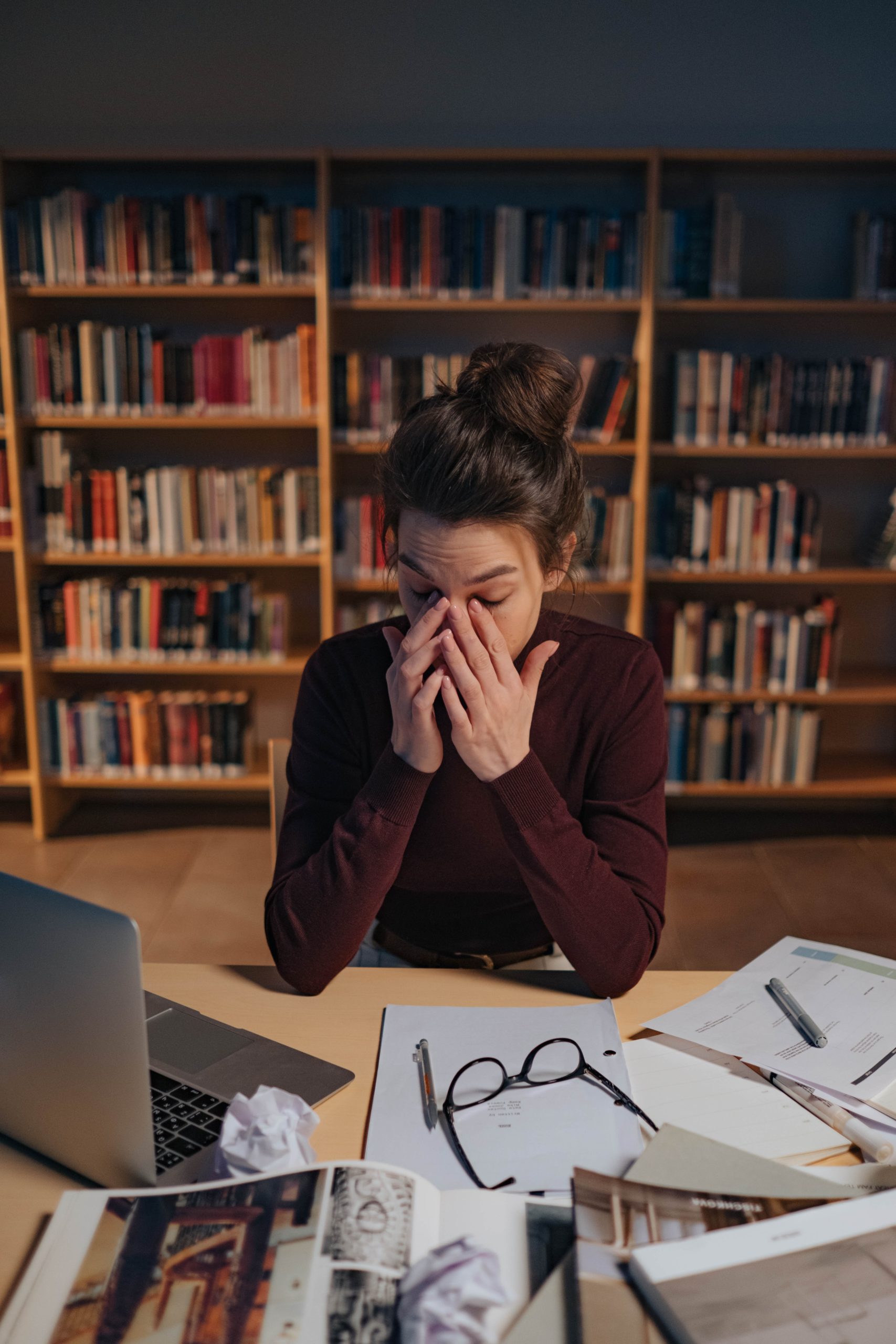 person sitting at a desk with a laptop and papers in front of them looking stressed at the work they are doing.